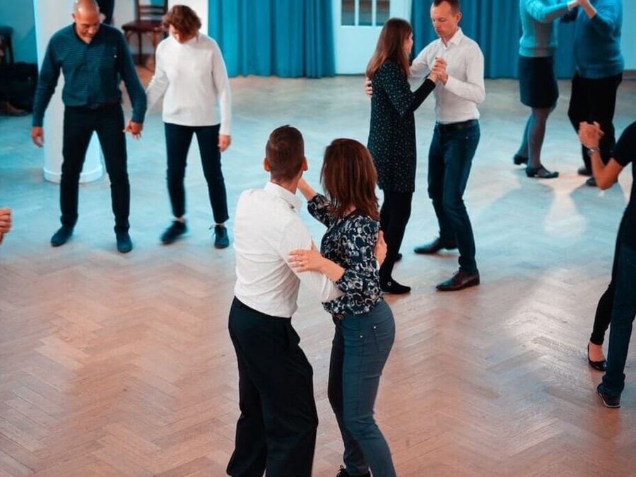 Couples dance tango in a bright hall with a parquet floor at BE-TANGO.
