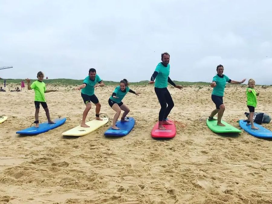 Children and adults practise standing up on surfboards laid out on the sand.
