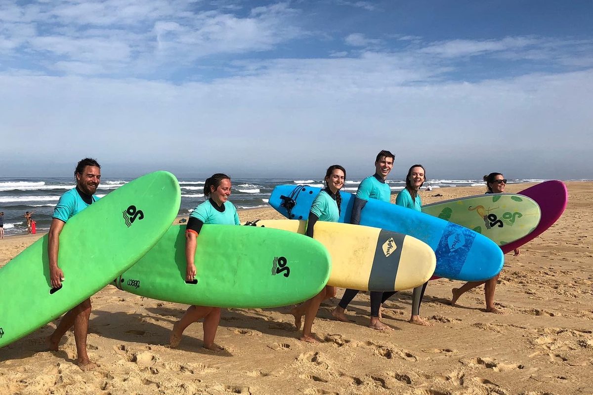 Smiling surf students carry their boards along the beach.